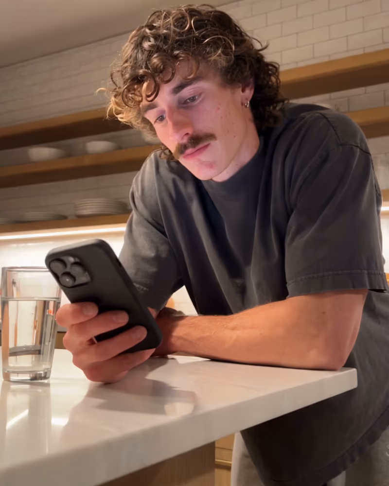 A person checking their phone at a warm, sunlit kitchen counter